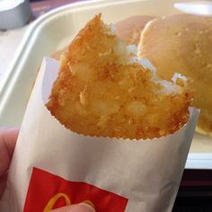 a person holding up a piece of food in front of a plate with buns