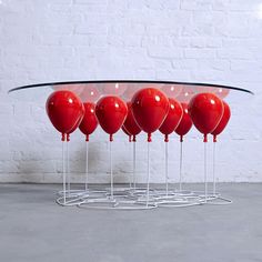 a glass table topped with red balloons on top of metal stand legs in front of a white brick wall