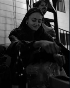 two people sitting down and one is pouring something into a glass in front of her