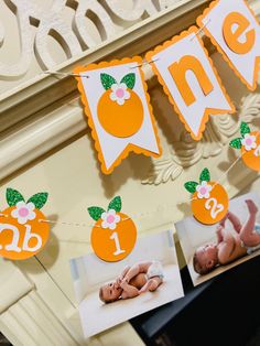 an orange and white banner is hanging from a mantel with baby pictures on it