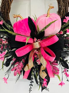 a wreath with pink and black flowers on the front door is decorated with two pumpkins