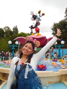 a woman standing in front of a fountain with mickey mouse on top