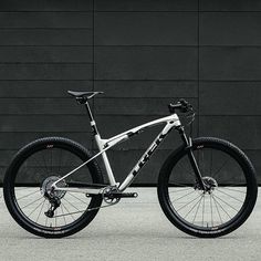 a white mountain bike parked in front of a black building with no wheels on it