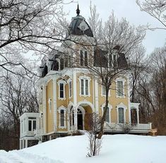 a large yellow house sitting on top of a snow covered hill in the middle of winter