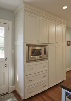 a kitchen with white cabinets and an oven in the center, along with hardwood flooring