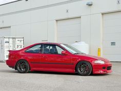 a red car is parked in front of a storage area with two doors and one door open