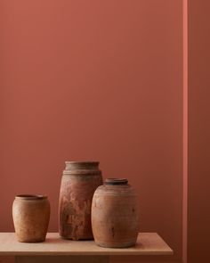 three vases sitting on top of a wooden table against a red wall in an empty room