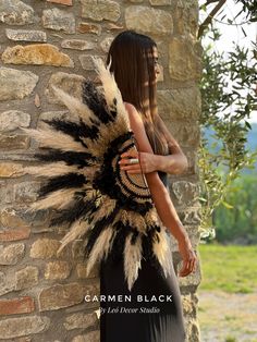 a woman standing next to a brick wall wearing a black and white feather headdress