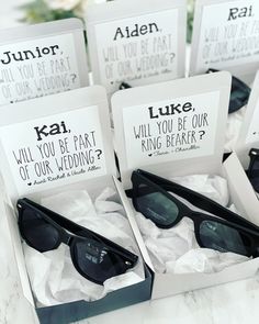 four pairs of sunglasses in boxes on top of a marble table with white cards reading will you be part of our wedding?