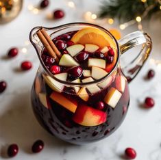 a glass pitcher filled with fruit and cinnamon on top of a white table next to christmas decorations