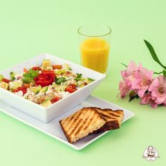 a bowl of salad next to a glass of orange juice on a green surface with pink flowers