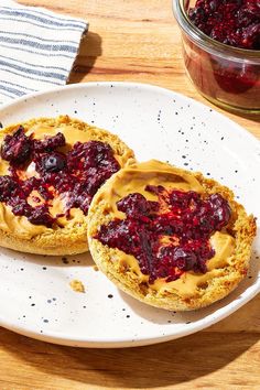 two pieces of bread with peanut butter and cranberry toppings on them sitting on a white plate