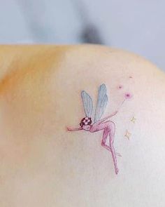 a small tattoo on the back of a woman's shoulder with a pink and blue fairy