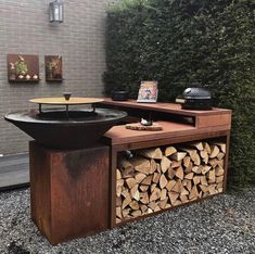 an outdoor fire pit with wood stacked on top and a grill in the back ground