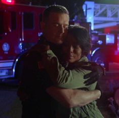 a man and woman hugging in front of a fire truck at night with their arms around each other