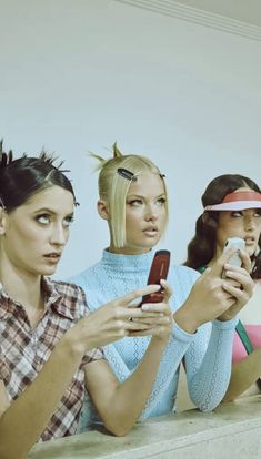 three women sitting next to each other while looking at their cell phones in front of them