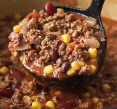 a spoon full of chili and ground beef with corn on the cob in it