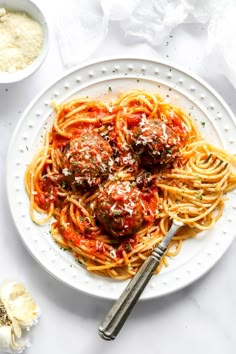 spaghetti with meatballs and marinara sauce in a white bowl on a white table