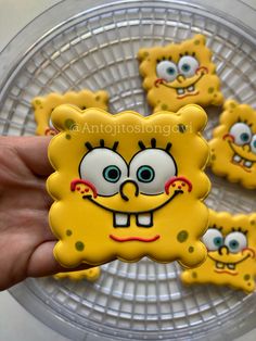 a person holding up some yellow cookies with faces on them in front of a plate