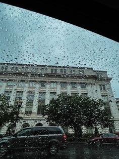 cars are parked on the street in front of a building with many windows covered by rain