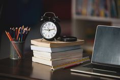 an alarm clock sitting on top of a stack of books next to a laptop computer