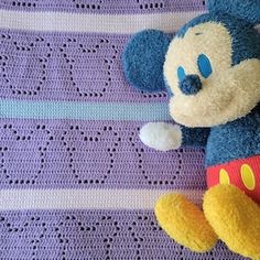 a blue and yellow teddy bear laying on top of a purple crocheted blanket