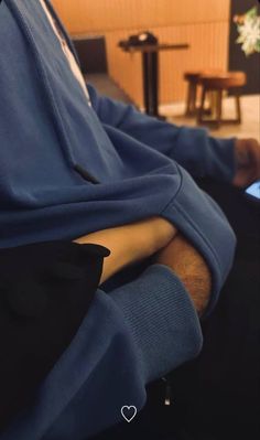 a man with his arm wrapped in a blue sweatshirt sitting on a couch next to a coffee table