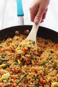 someone is stirring rice in a skillet with a wooden spatula on the side