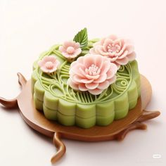 a green cake with pink flowers on top sitting on a wooden platter next to a white wall