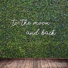 the words to the moon and back are written on top of a green hedge wall