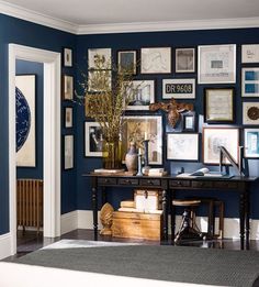 a home office with blue walls and lots of framed pictures on the wall above it