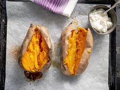 two baked potatoes sitting on top of a baking pan next to a bowl of whipped cream