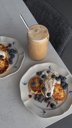 two white plates topped with pancakes and blueberries next to a cup of iced coffee