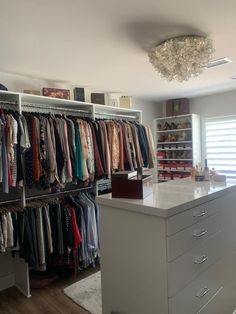 an organized closet with clothes hanging on shelves and drawers, along with a chandelier