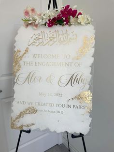 a welcome sign with flowers on it in front of a white door that says, welcome to the engagement of alex and ally