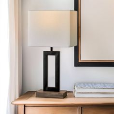 a lamp sitting on top of a wooden table next to a mirror and a book