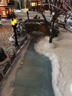 a small pond in the middle of a snow covered yard with trees and lights on either side