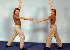 two people standing in front of a white wall with their arms stretched out to each other