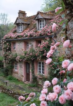 an old stone house with pink flowers growing on it