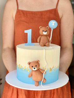 a woman holding a cake with two teddy bears on it and the number one on top