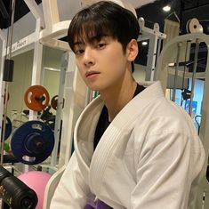 a young man in a kimono sitting on a bench with dumbbells behind him