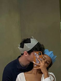 a man and woman taking a selfie in front of a mirror wearing paper crowns