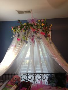 a canopy over a bed with flowers hanging from it's side and stuffed animals on the floor