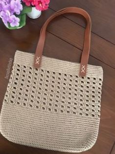 a crocheted bag sitting on top of a wooden table next to purple flowers