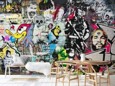 a wall covered in lots of graffiti next to two wooden chairs and a small table