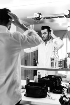 a man standing in front of a mirror while getting his hair combed by another man