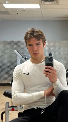 a young man sitting in a gym holding a cell phone and looking at the camera