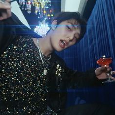 a young man holding a drink in his right hand and wearing a sequin shirt