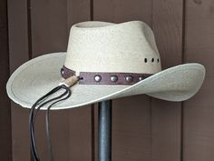 Chet starts with a Mexican soft palm leaf hat body that has a 3 3/4" brim and 5 1/4" crown. The band is simple with distressed brown leather and antique nickel color spots. The back of the band has a deer antler bead for accent. A neutral feather combo completes the hat. Note: Please allow 3-4 weeks. Rustic Adjustable Short Brim Hat, Rustic Adjustable Brimmed Hat, Rustic Adjustable Hats For Rodeo, Rustic Adjustable Hat With Curved Brim, Adjustable Western Straw Hat For Kentucky Derby, Adjustable Natural Straw Hat For Ranch, Adjustable Wide Brim Rustic Fedora, Rustic Brown Hat With Flat Crown, Rustic Curved Brim Hat Bands For Rodeo