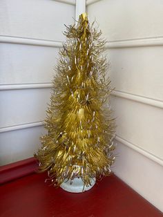 a gold tinsel christmas tree sitting on top of a red table next to a white wall